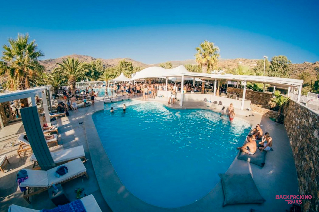 Guests enjoy the vibrant pool area at a hotel in Ios, with palm trees and clear blue skies.
