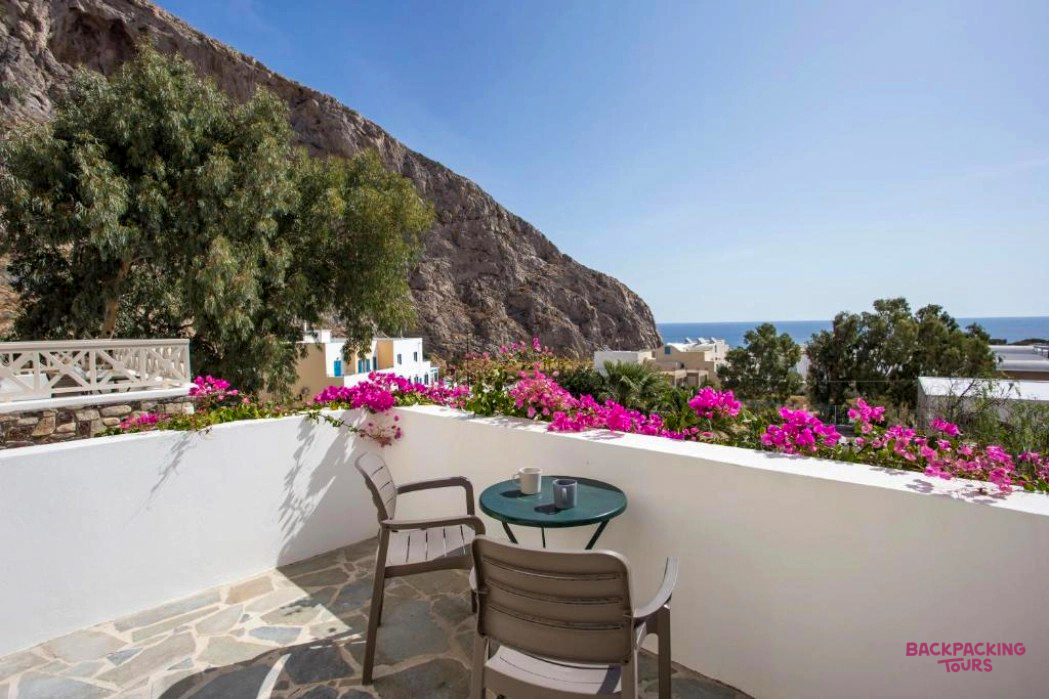 A sunny balcony with pink flowers, two chairs, and a table overlooking the sea in Santorini.