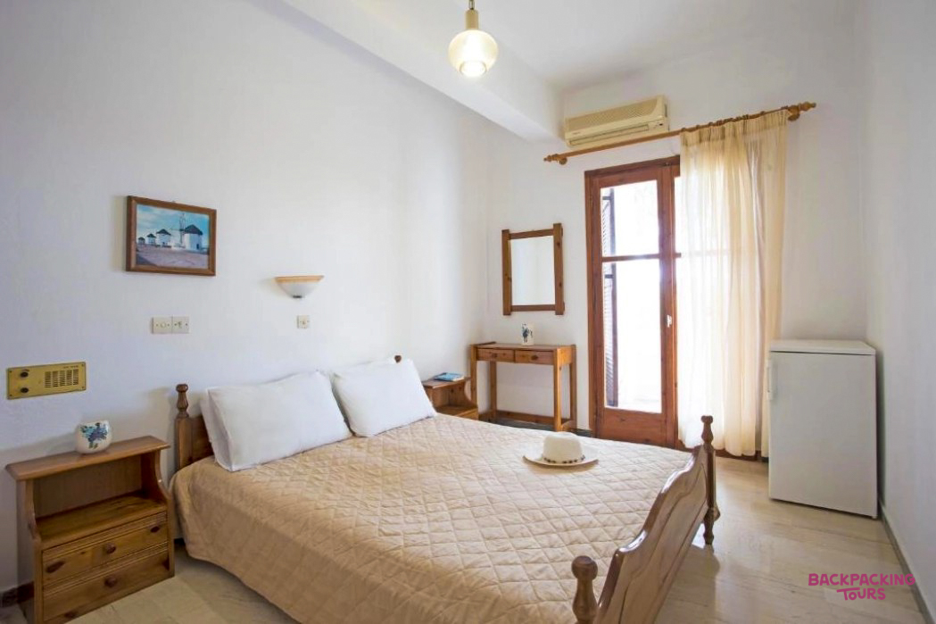 A bright and inviting double room in Santorini, featuring a wooden bed and simple decor.