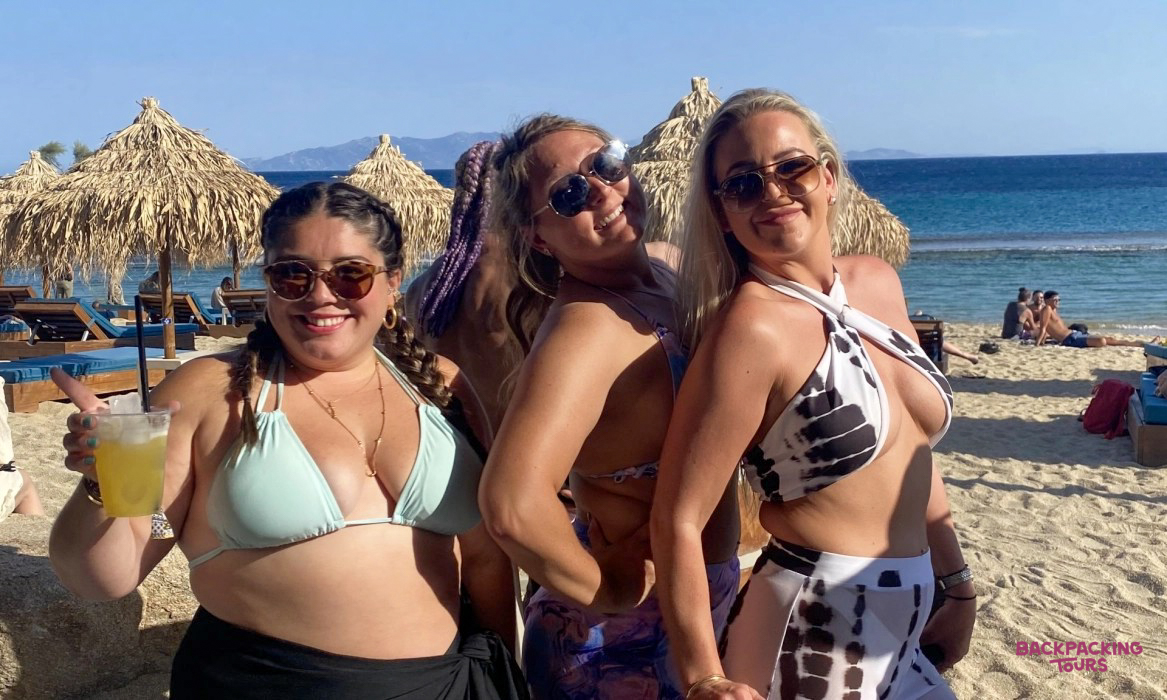 Three cheerful women enjoying the sun and drinks at a lively beach club in Mykonos.