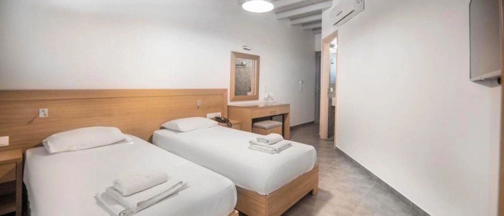 A clean and bright hotel room in Ios with two single beds and white linens.