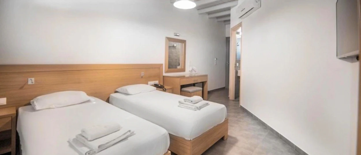 A clean and bright hotel room in Ios with two single beds and white linens.