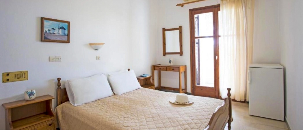 A simple, bright hotel room in Santorini with a double bed and a painting of island architecture.
