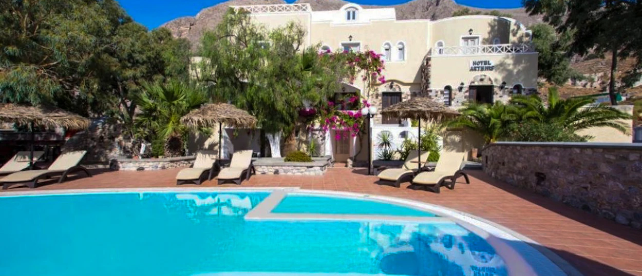 Relaxing swimming pool area with sun loungers and straw umbrellas at a traditional hotel in Santorini.