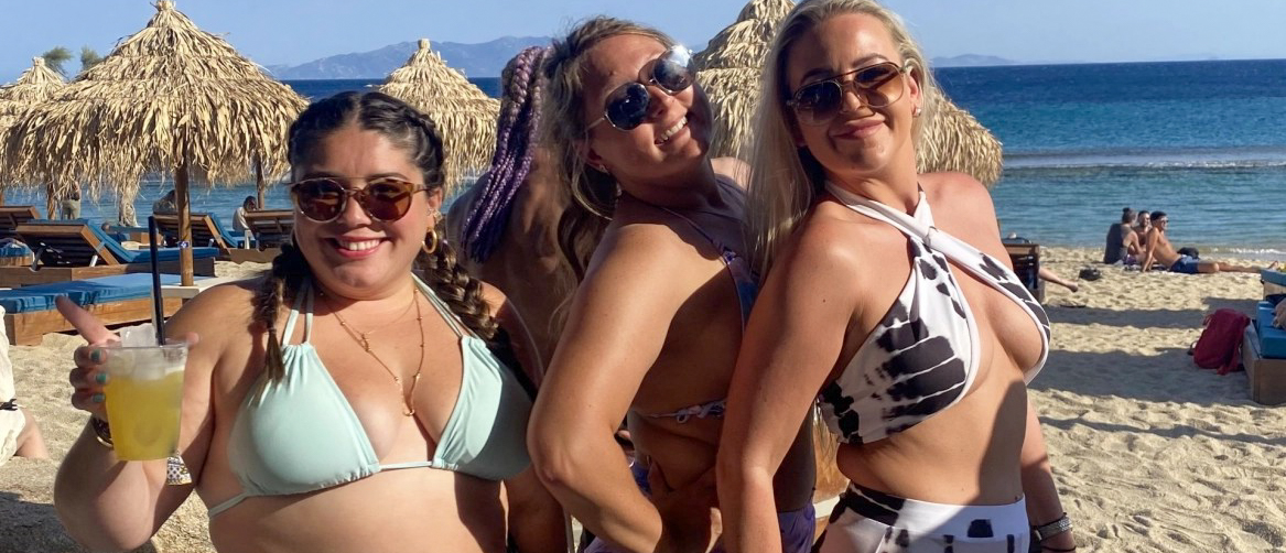 Three happy women enjoy cocktails and sunshine at a vibrant beach club in Mykonos.