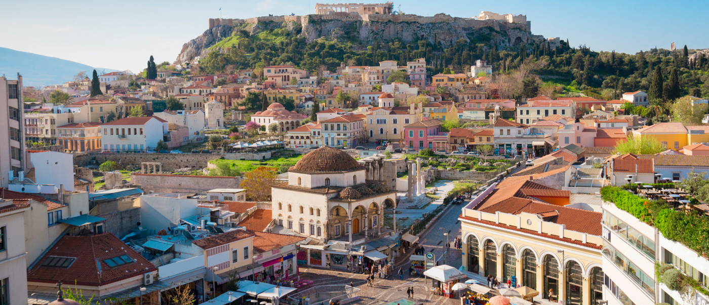 A vibrant city scene in Athens with historic buildings and the grand Acropolis on a green hill.