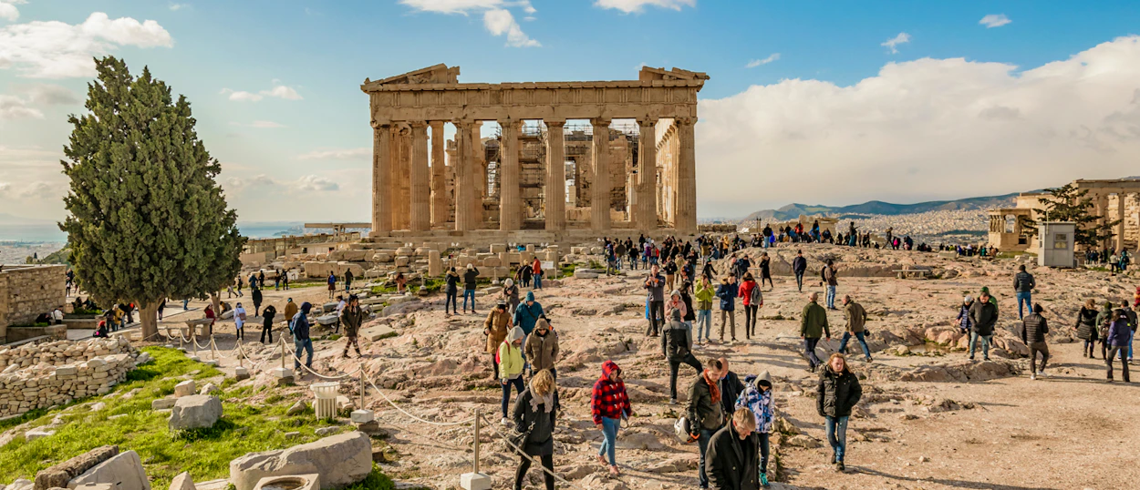 Tourists explore the ancient ruins of the Parthenon on the sunny Acropolis in Athens.