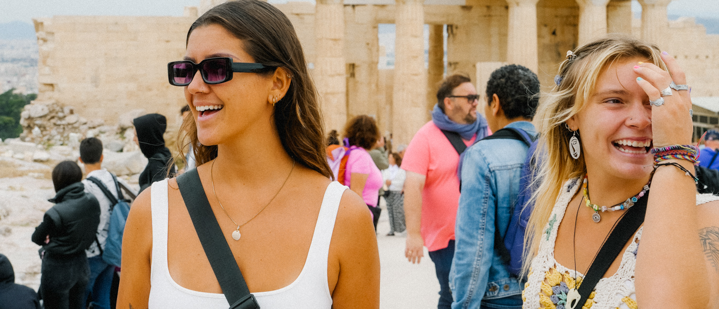 Two joyful women smiling and laughing while exploring ancient Greek ruins in Athens.
