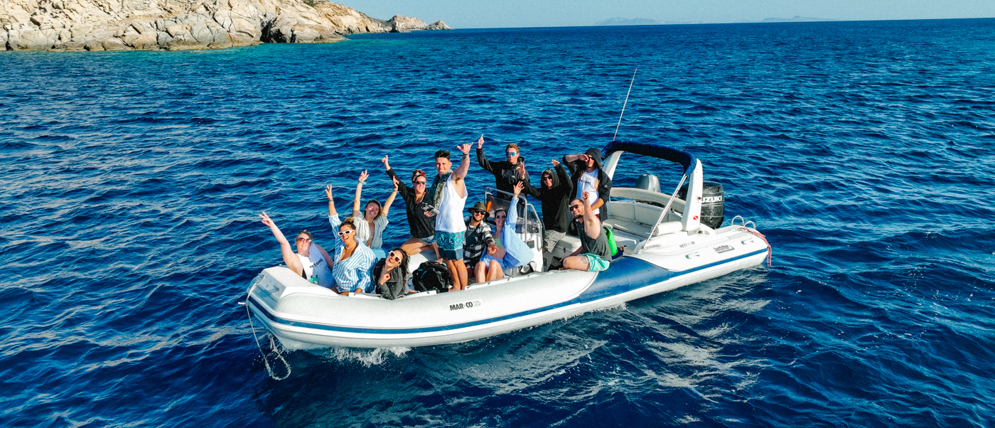A group of happy friends waving from a speedboat on the blue sea near Ios, Greece.
