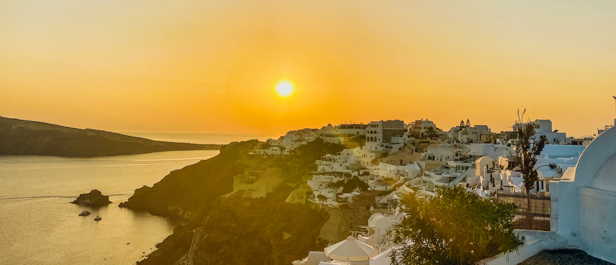 A golden sunset over the white-washed cliffside village of Oia, Santorini, overlooking the Aegean Sea.