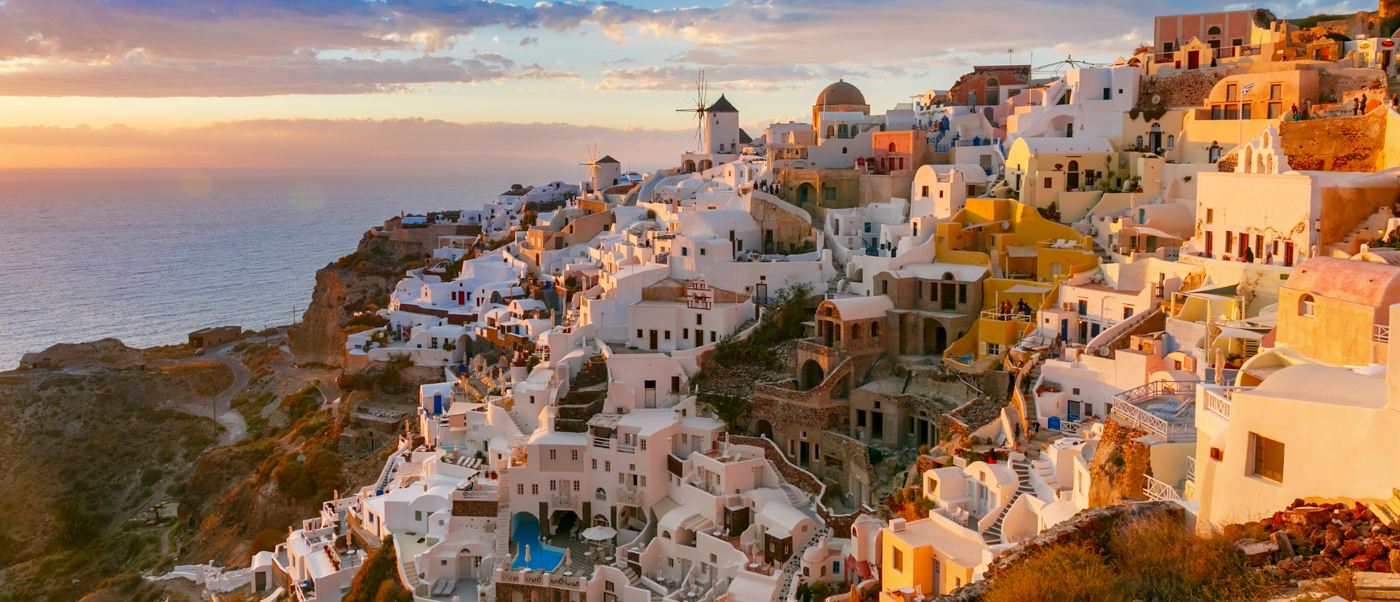 White cliffside village of Oia, Santorini, glowing golden at sunset over the Aegean Sea.