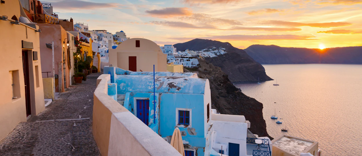 Golden sunset over the iconic white and blue buildings of Santorini, overlooking the calm Aegean Sea.