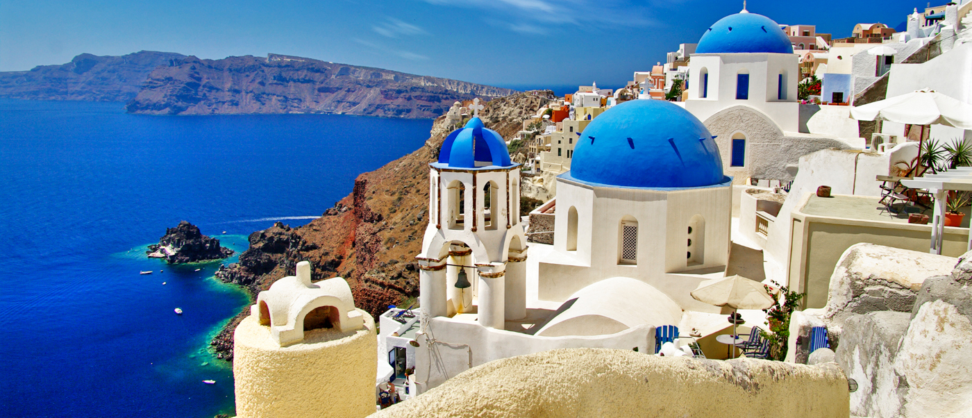 White buildings with blue domes overlooking the deep blue caldera of Santorini.