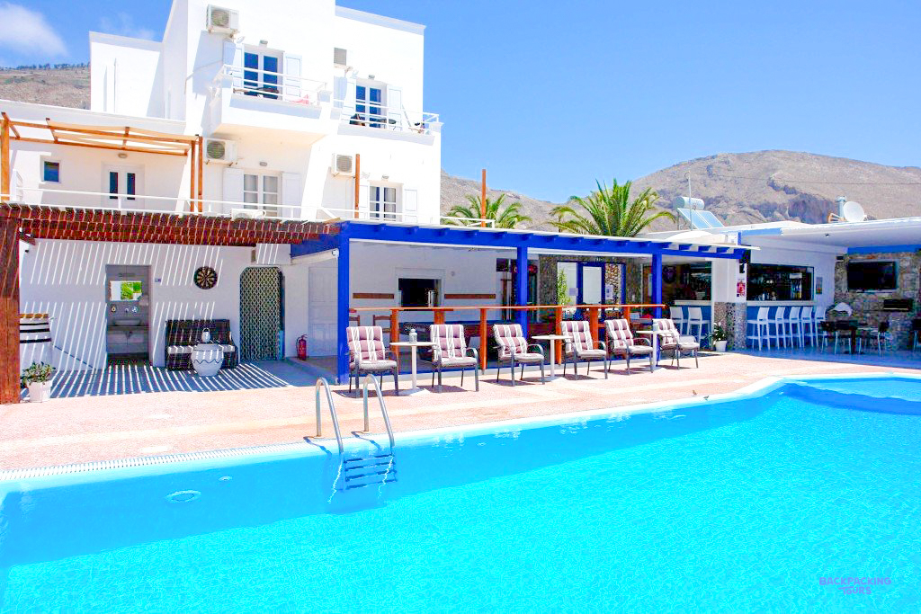 The swimming pool and sun loungers beside the white Kalipso Villas building in Santorini