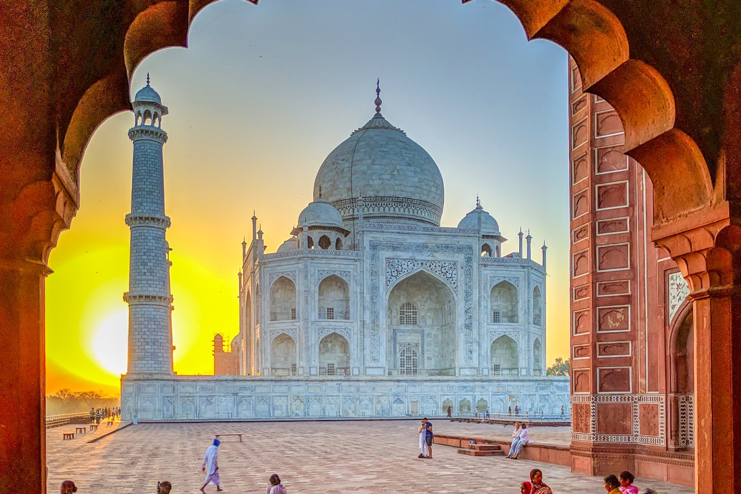 Visitors admire the magnificent Taj Mahal at sunrise, framed by an ornate archway in Agra.