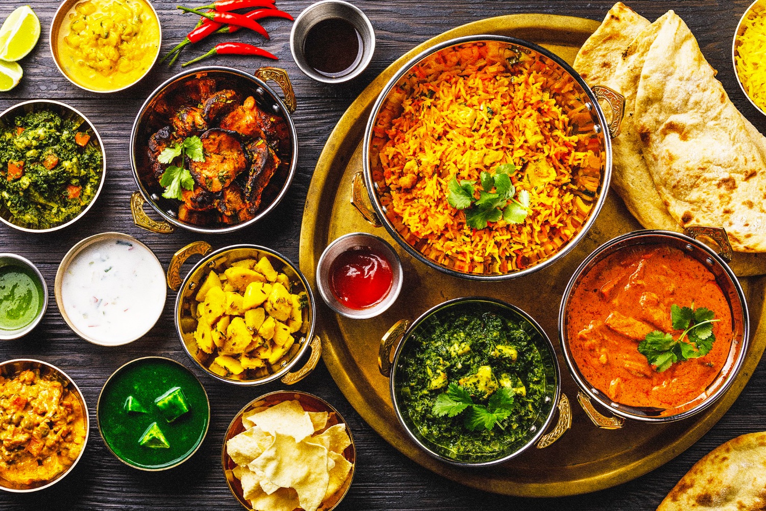 A vibrant spread of traditional Indian dishes including curries, rice, and flatbread on a wooden table.