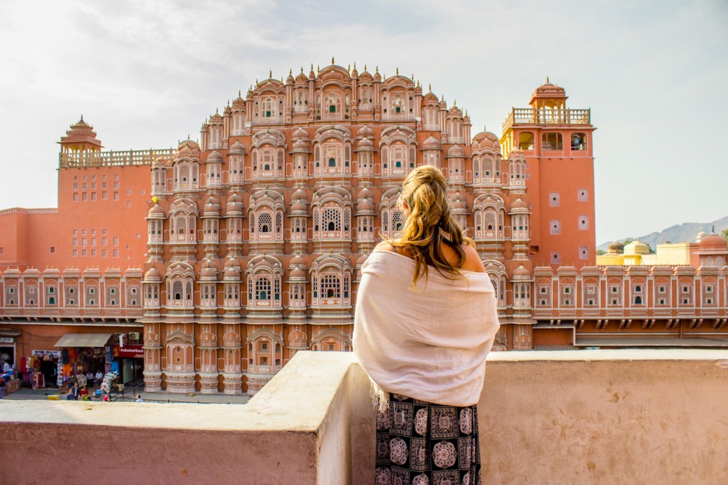Woman in a white shawl admiring the intricate pink Hawa Mahal palace in Jaipur, India.