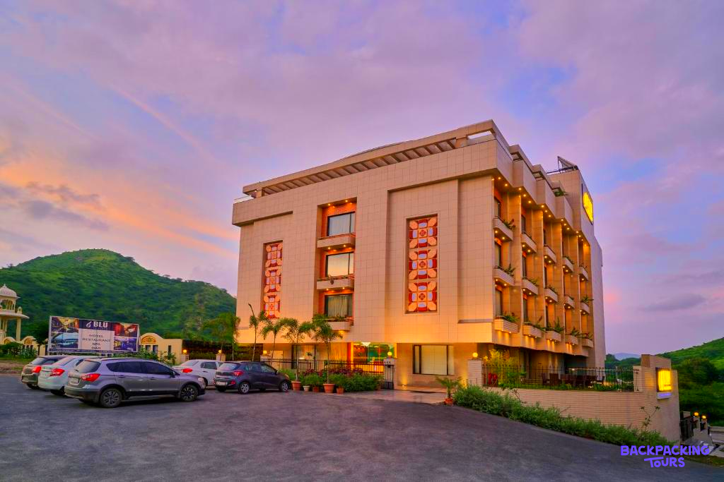 A modern hotel building in Udaipur with warm lights under a beautiful pink and purple sunset sky.