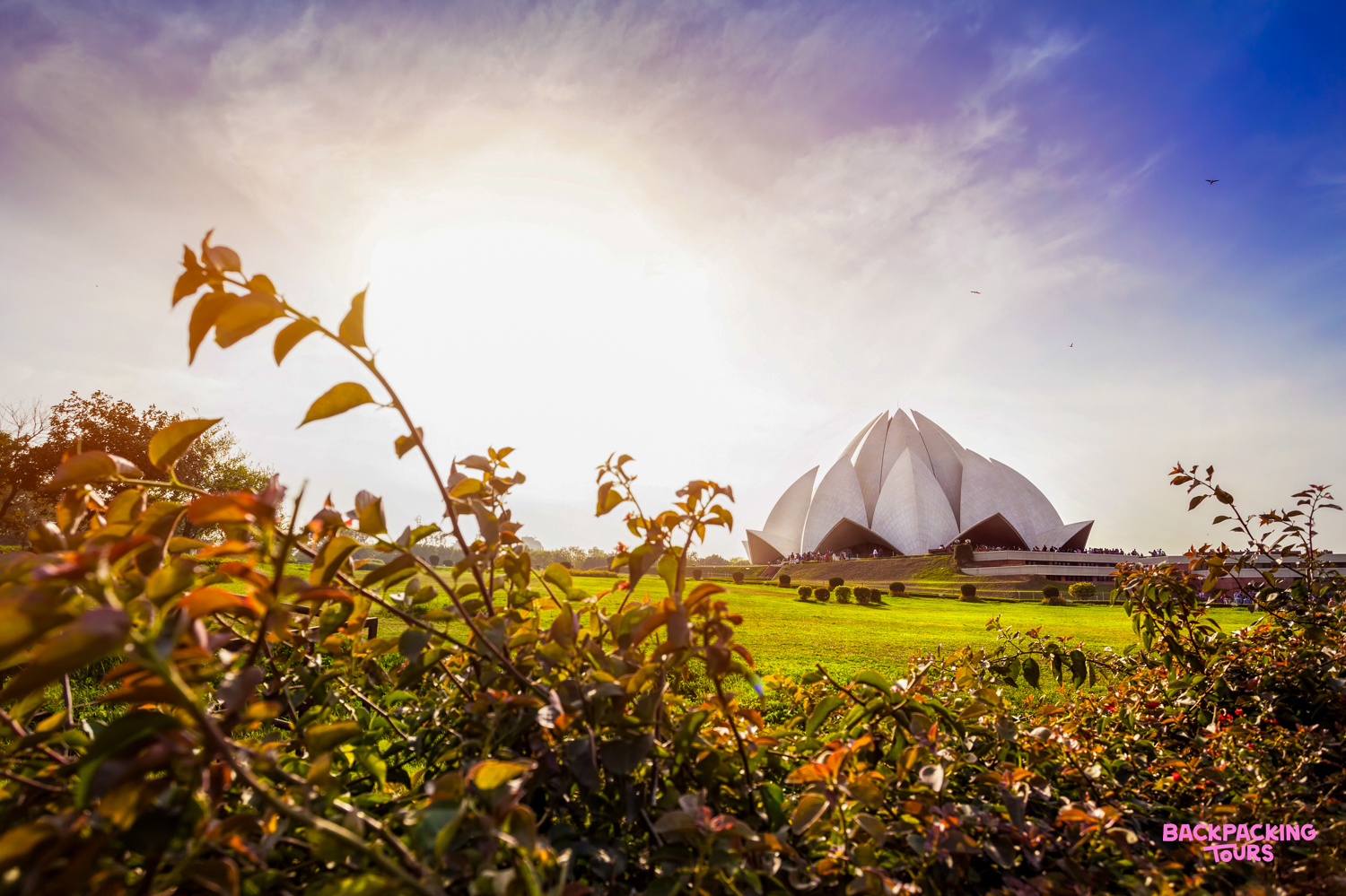 The iconic Lotus Temple in New Delhi stands majestically amidst lush green gardens under a bright sun.