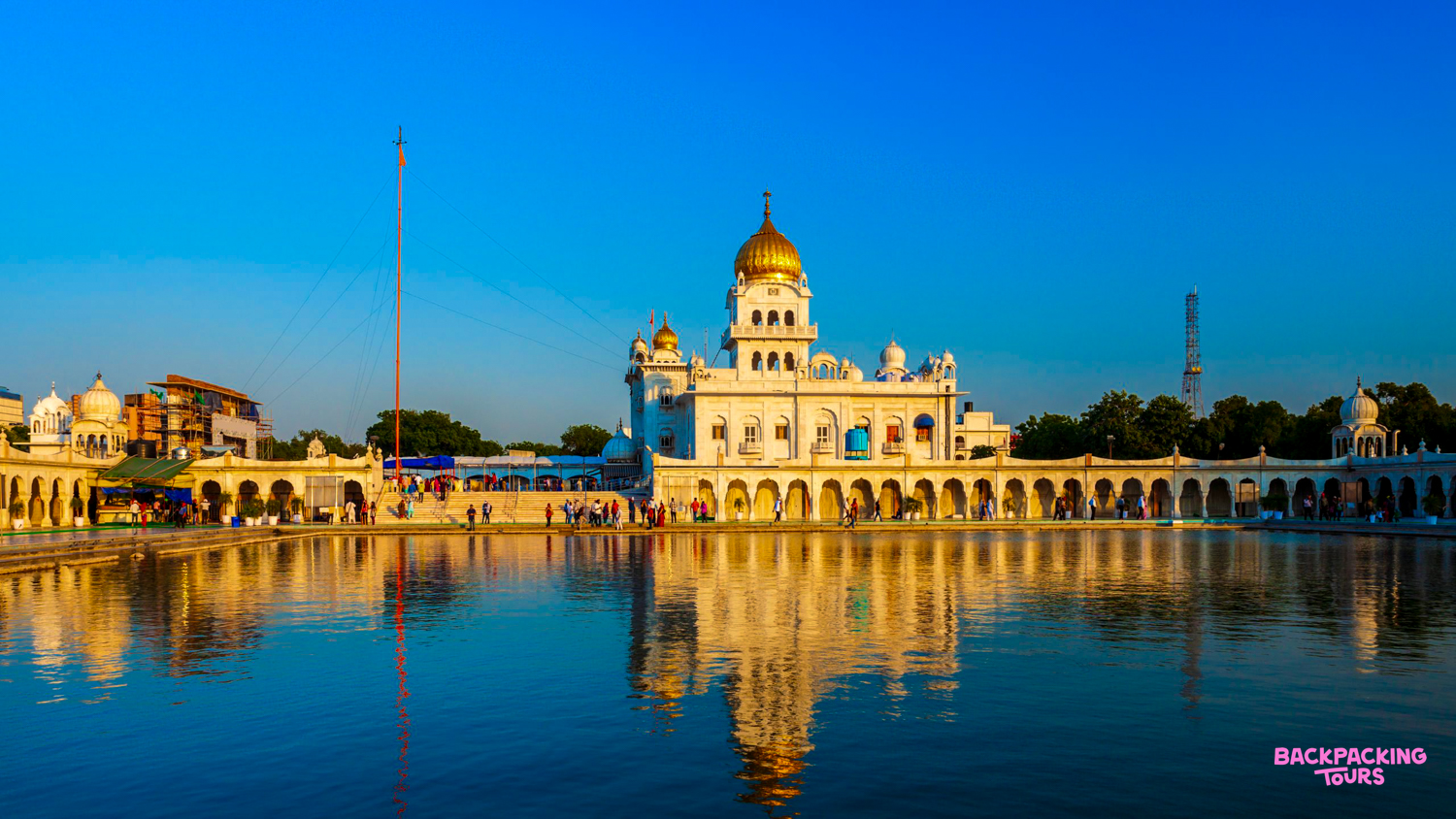 The stunning white Sikh temple with golden domes reflects beautifully in a tranquil pond in New Delhi.