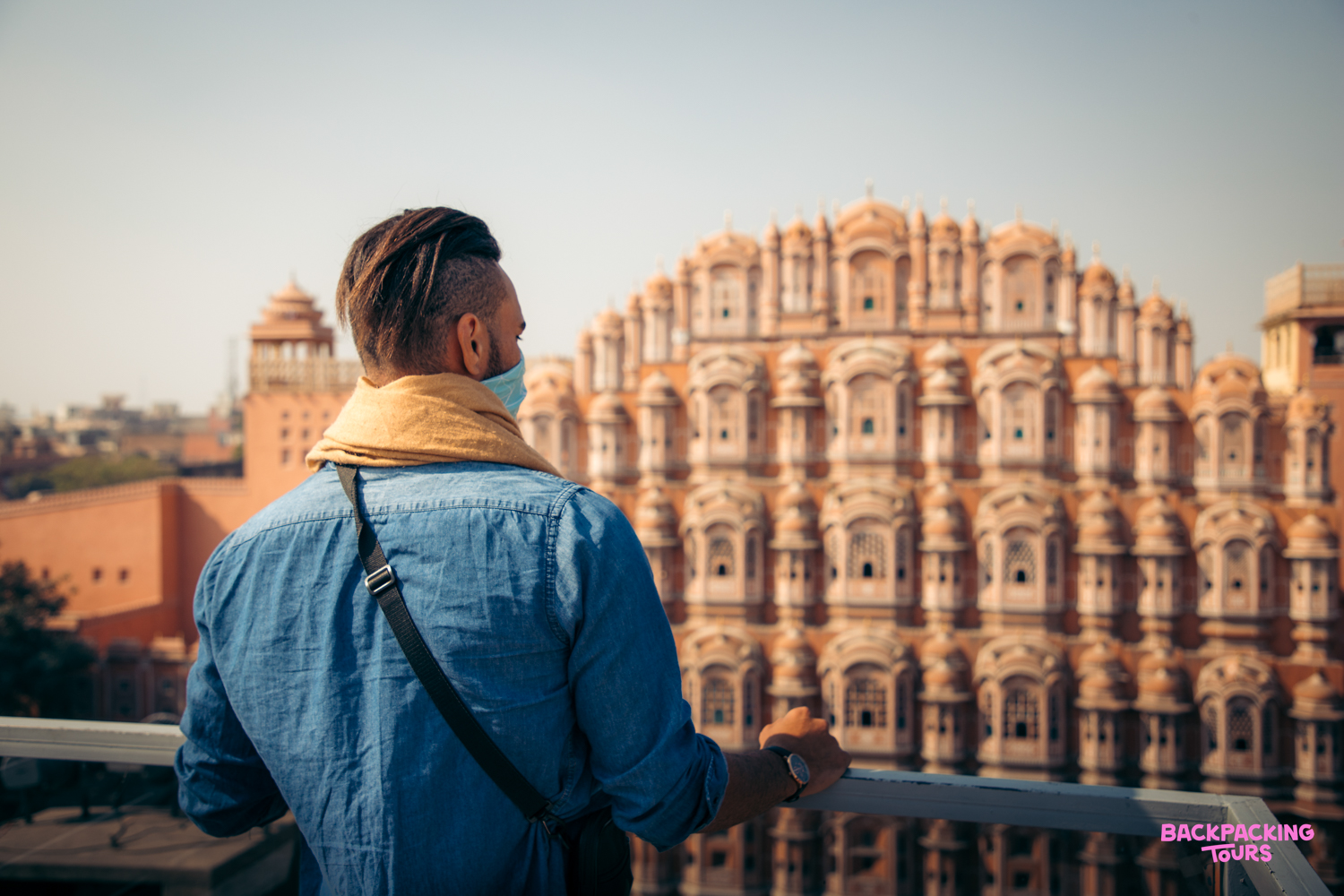 A traveler wearing a mask admires the intricate pink facade of the Hawa Mahal in Jaipur.