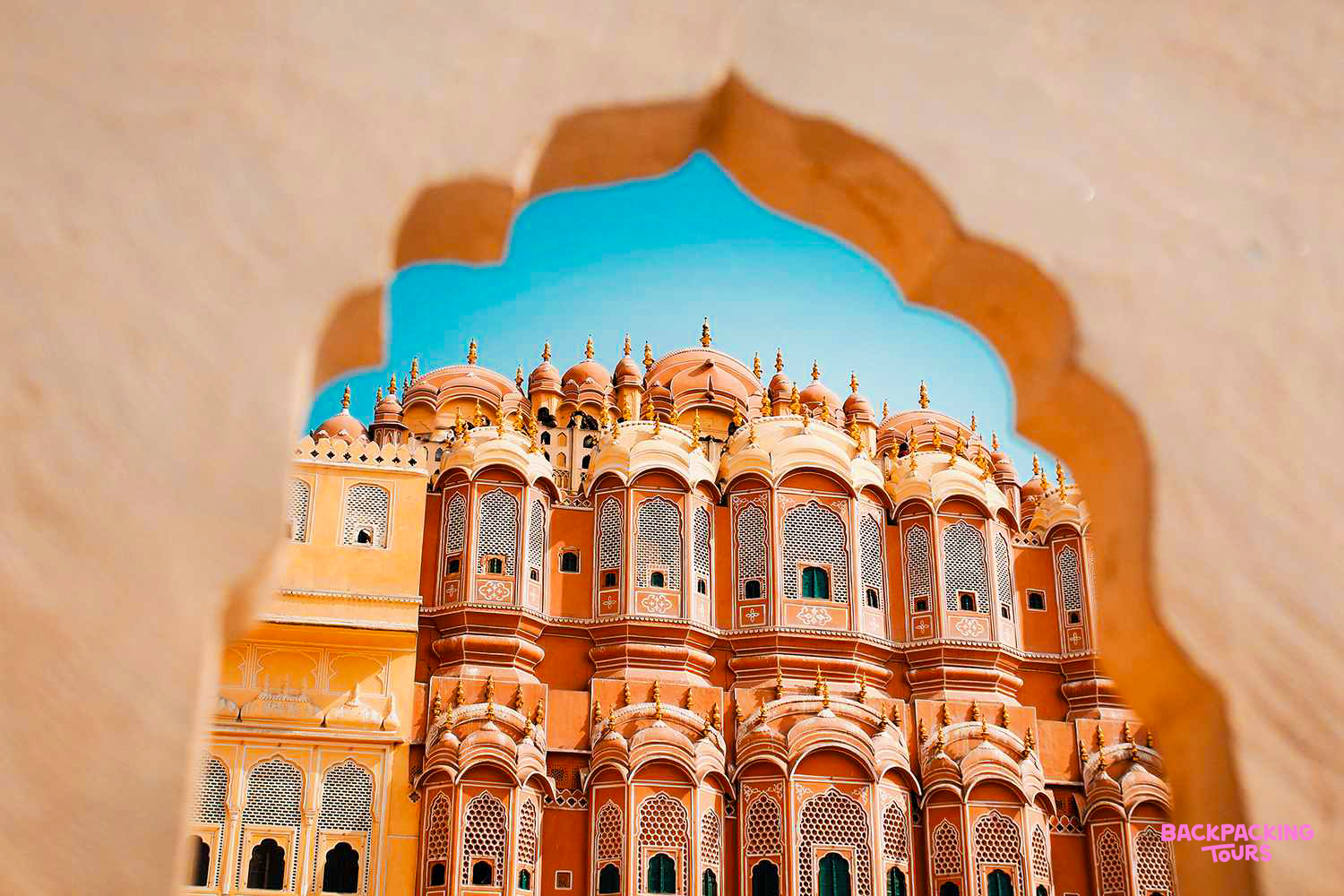 The stunning pink Hawa Mahal in Jaipur, India, with its many windows and domes under a blue sky.