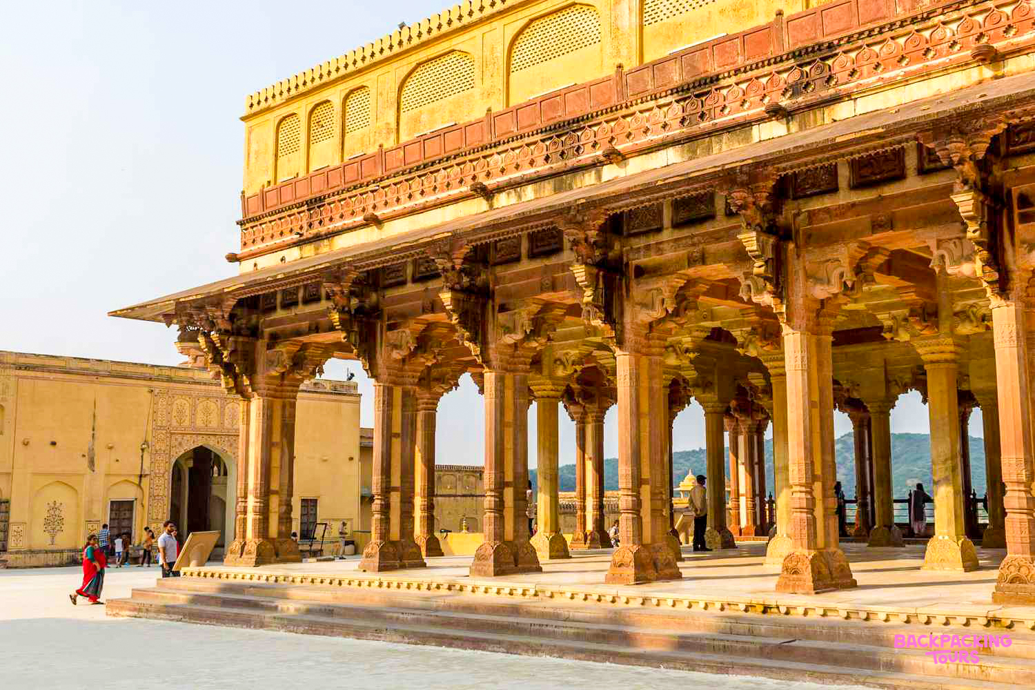 Tourists explore the grand, ornate Amber Fort in Jaipur, India, under a clear sky.