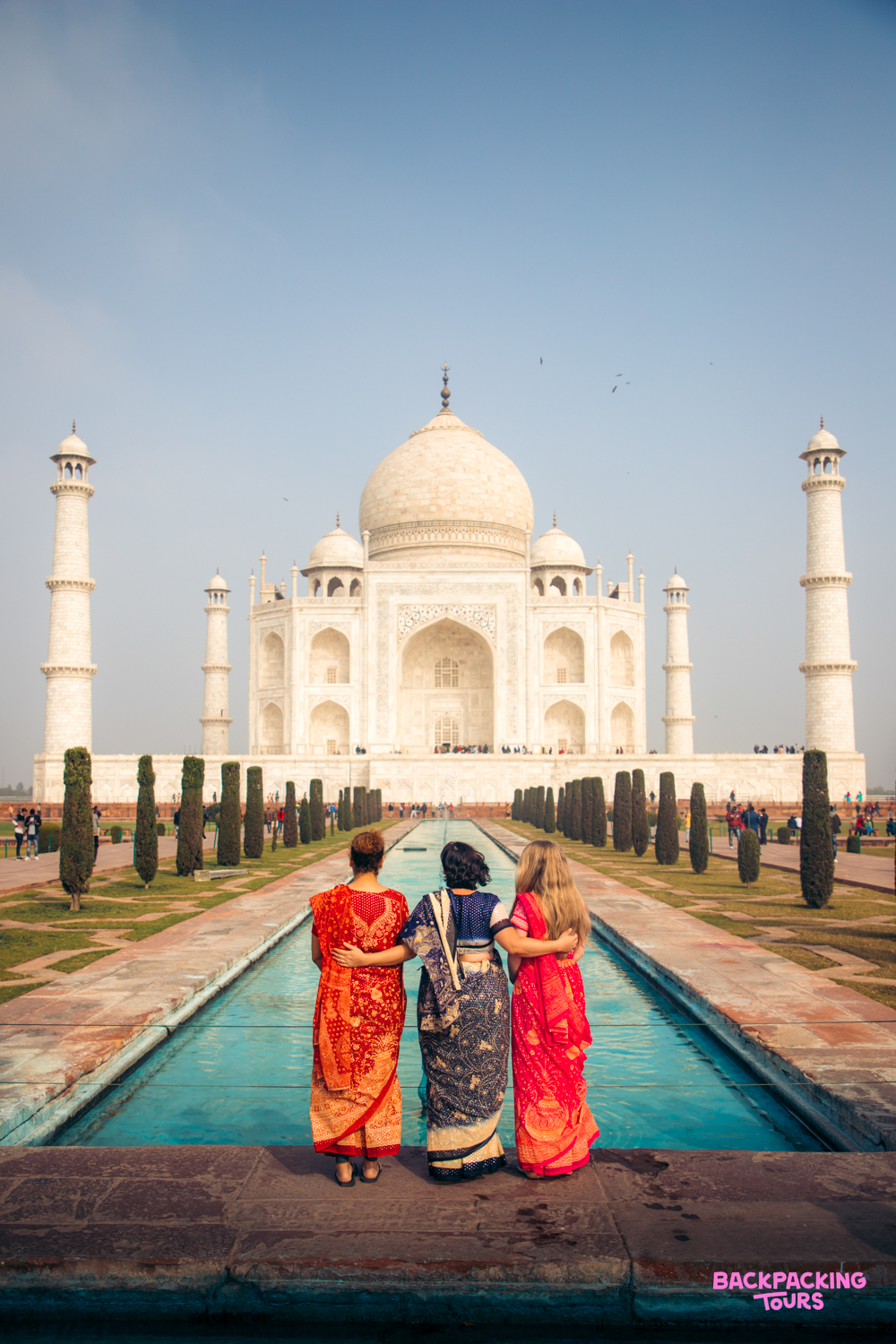 Three women in colorful saris admire the majestic Taj Mahal in Agra, India.