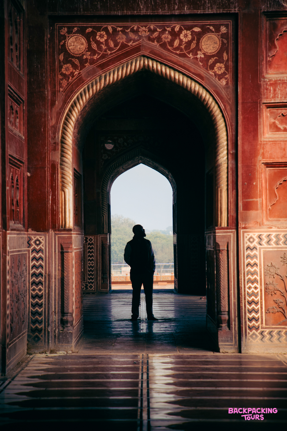 A person stands silhouetted in a grand, ornate archway at the Taj Mahal complex in Agra.