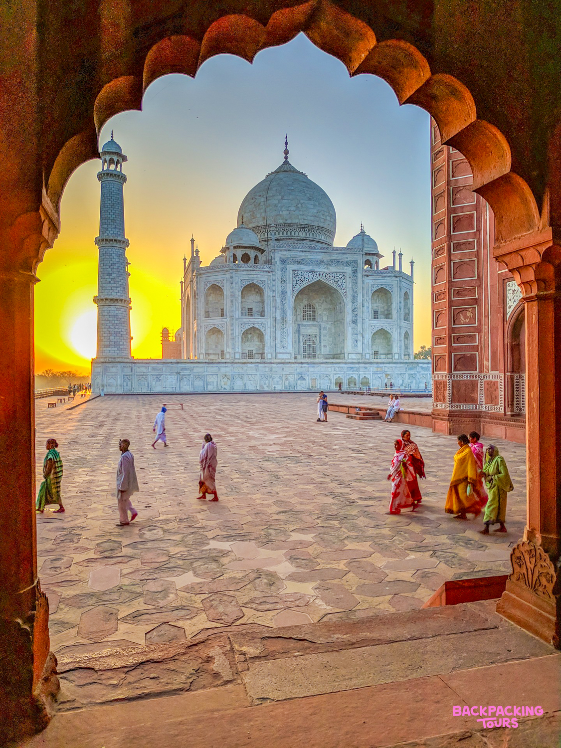 Visitors walk across the Taj Mahal courtyard at sunset, framed by a beautiful archway in Agra.