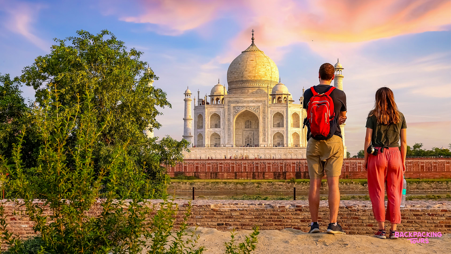 Two backpackers admire the majestic Taj Mahal at sunrise in Agra, India.