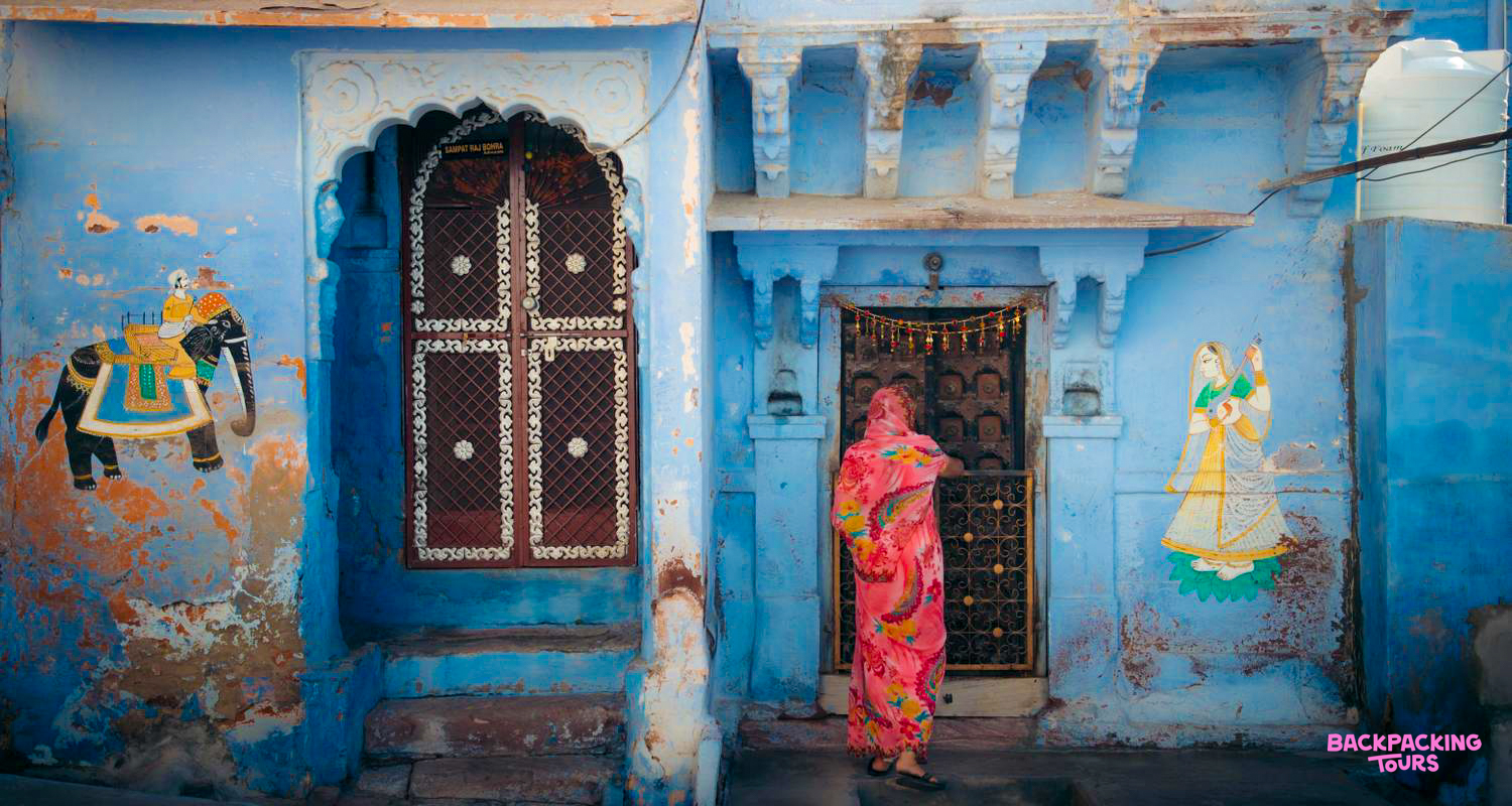 A woman in a bright pink sari approaches an ornate doorway in Jodhpur's famous blue city.