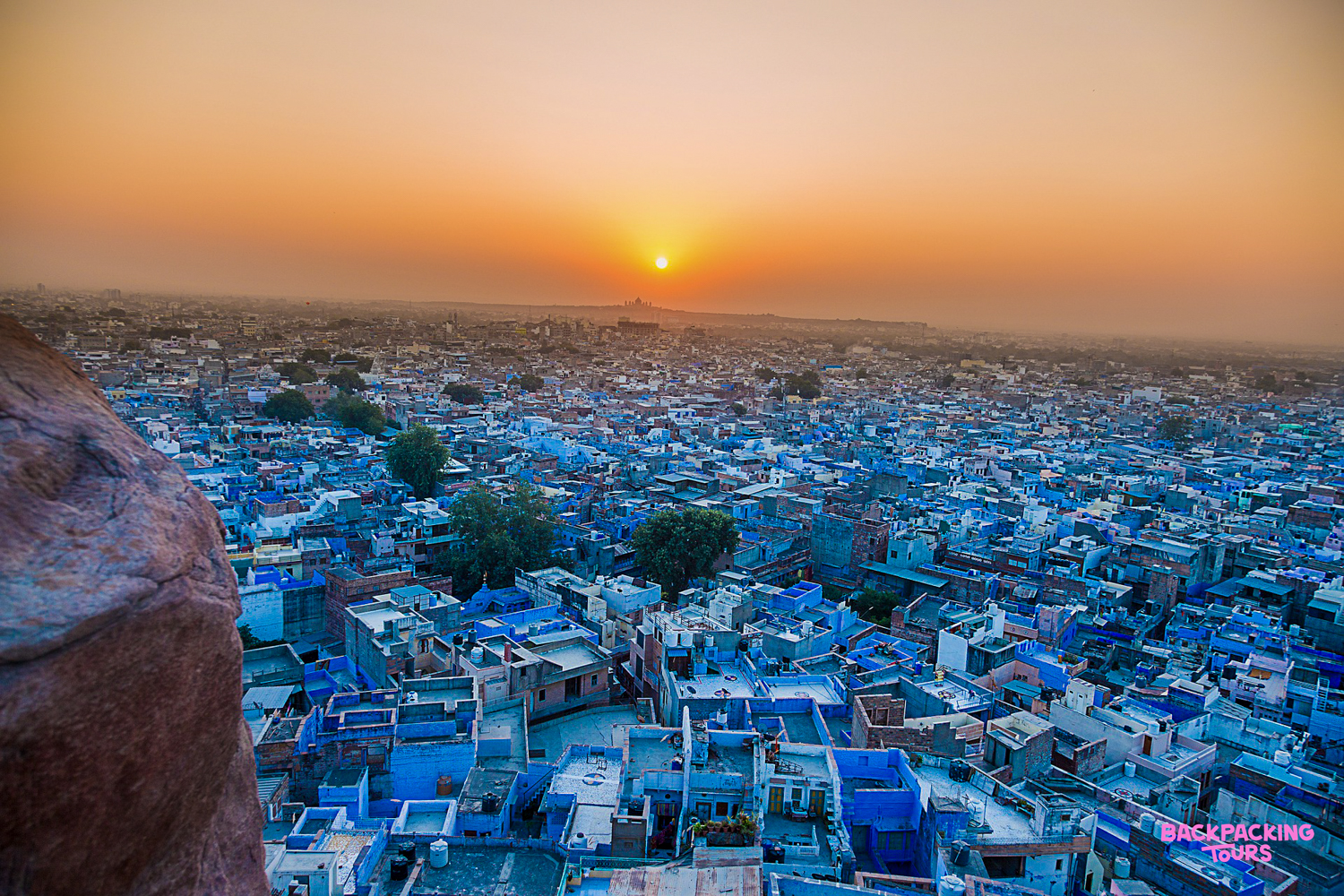 The vibrant blue buildings of Jodhpur stretch to the horizon under a beautiful sunset sky.