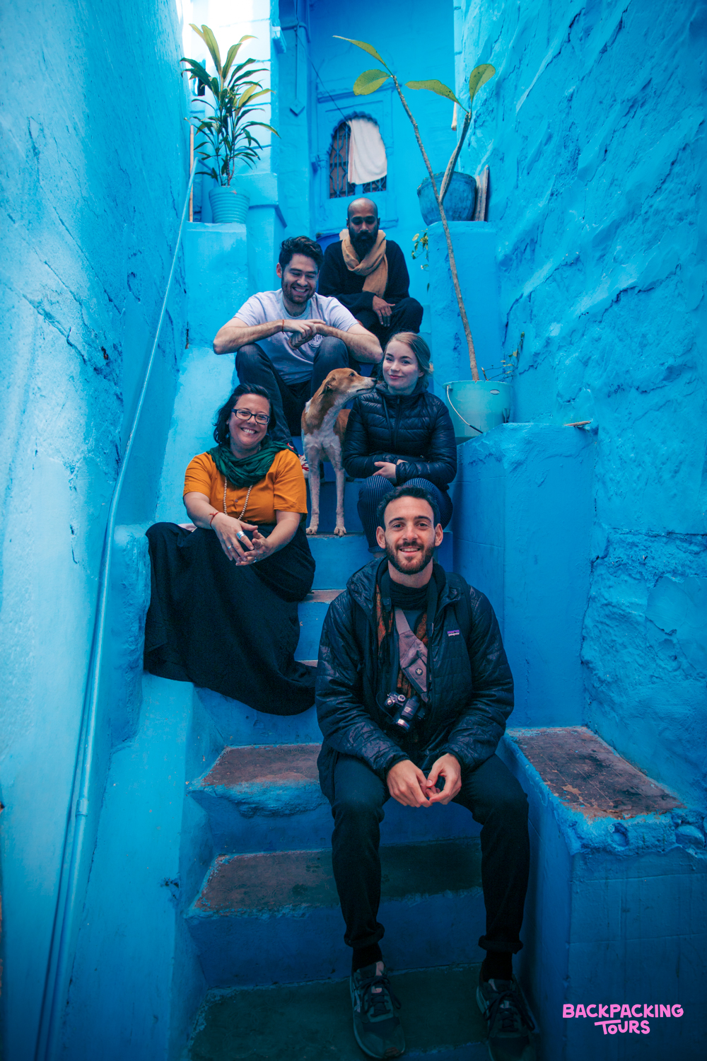 Smiling travelers and a dog pose on vibrant blue stairs in the charming city of Jodhpur.