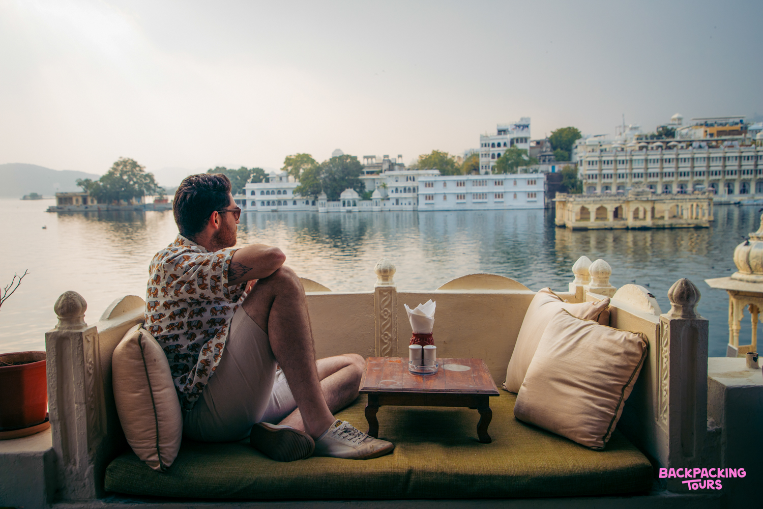 A man relaxes on a balcony, enjoying the serene Lake Pichola and palaces in Udaipur.