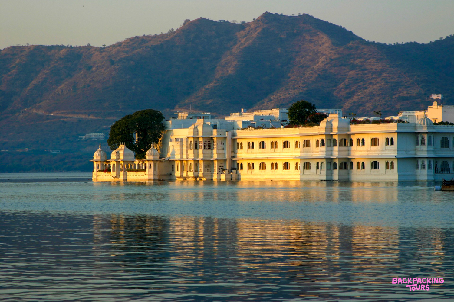 A majestic white palace on Lake Pichola in Udaipur glows under the warm golden sunset.