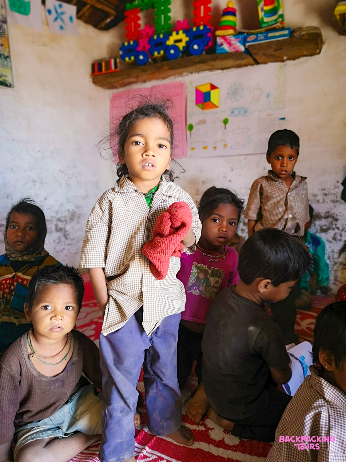 Curious young children in a simple room in Udaipur, India, with one child standing prominently.