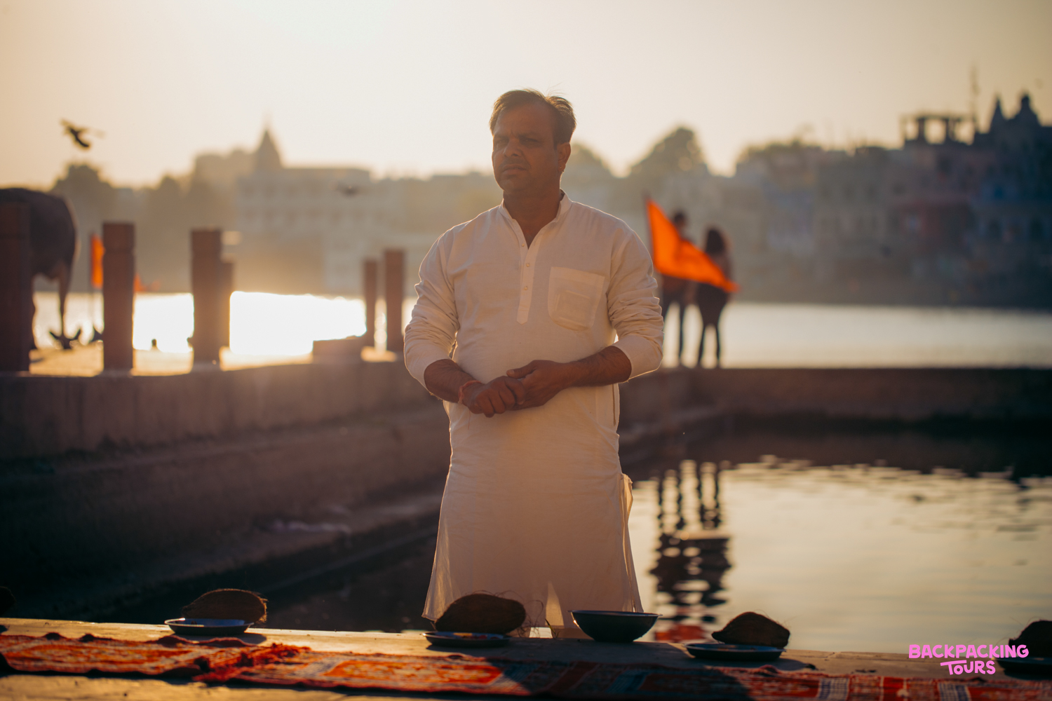 A Brahmin priest in white performs a blessing ceremony by the sacred Pushkar Lake at sunset.