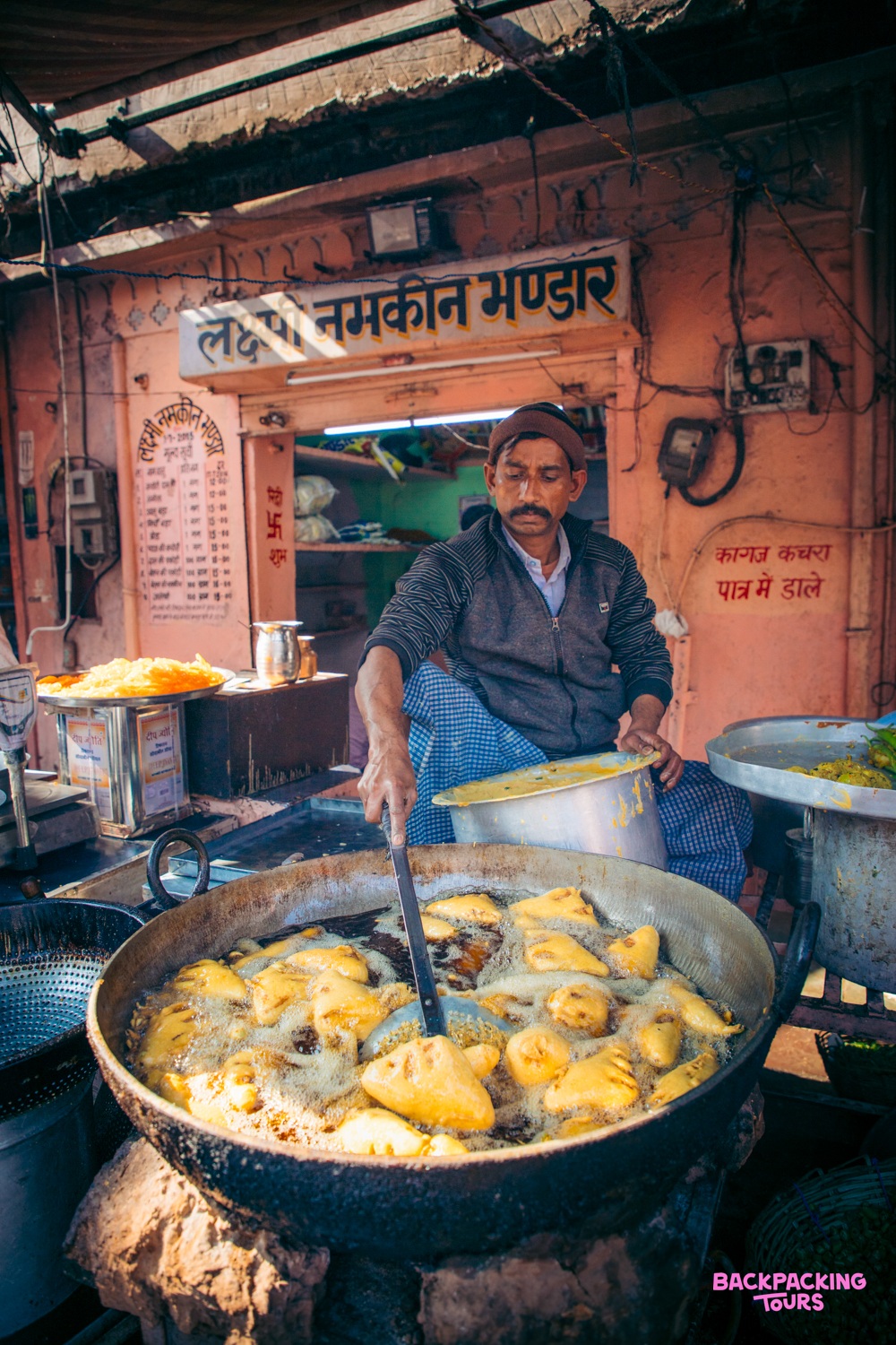 A man fries delicious-looking snacks in a large pot at a street food stall in India.