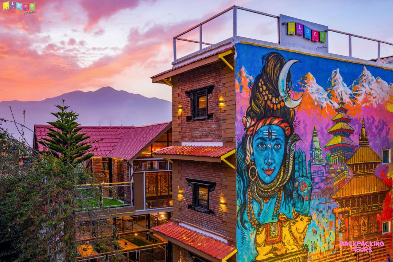 A vibrant hostel building in Kathmandu featuring a large mural and a beautiful sunset over distant mountains.