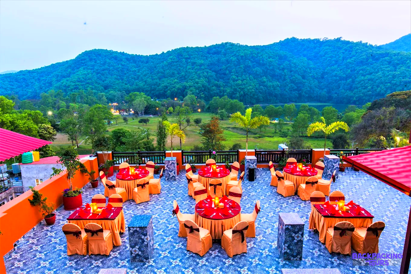 An inviting rooftop dining area with red and gold tables, overlooking the scenic Pokhara valley and lake.
