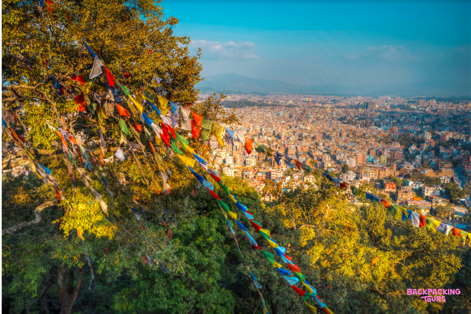 Colorful prayer flags flutter above the sprawling city of Kathmandu, Nepal, under a clear blue sky.