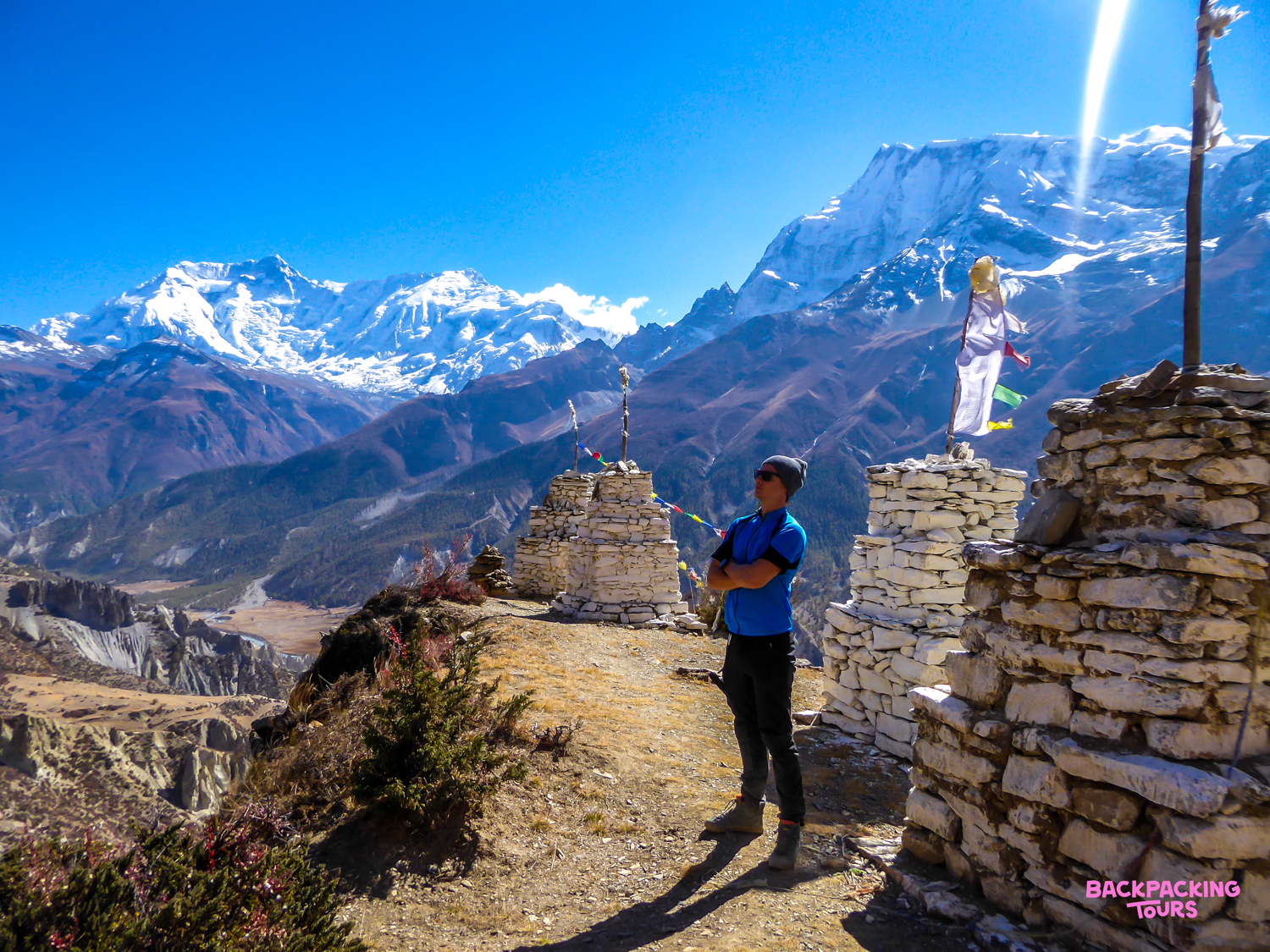 Backpacker enjoys the stunning vista of the Annapurna Range from Australian Camp, surrounded by stone structures.