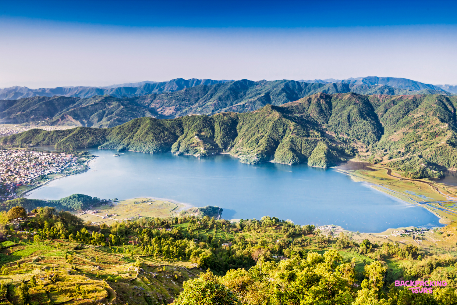 Panoramic view of Phewa Lake in Pokhara, Nepal, surrounded by green hills and a vibrant town.