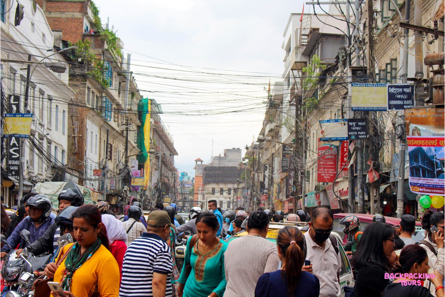 A bustling street in Kathmandu's Thamel Bazaar, with many people and motorbikes navigating the busy scene.
