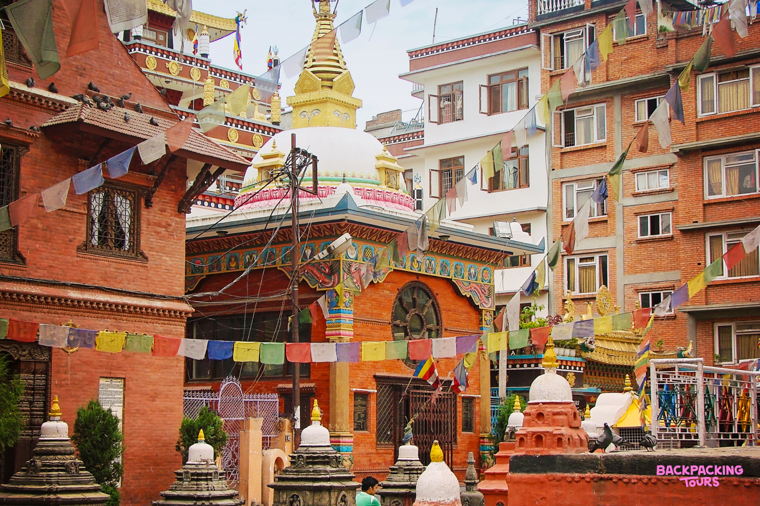 Colorful prayer flags adorn traditional Nepalese buildings and ornate stupas in a lively Kathmandu street.