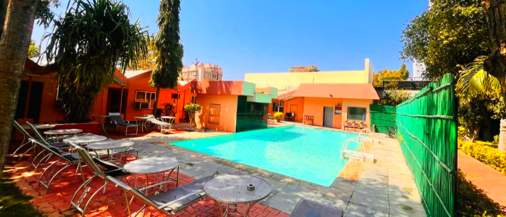 Bright outdoor swimming pool with orange buildings and empty lounge chairs on a sunny day in Pushkar.