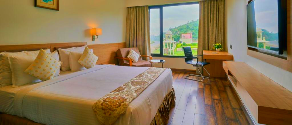 A comfortable hotel room with a large bed and a scenic view of white palaces in Udaipur.