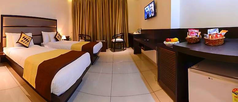 A well-appointed hotel room with two beds, a television, and a desk with snacks and fruit.