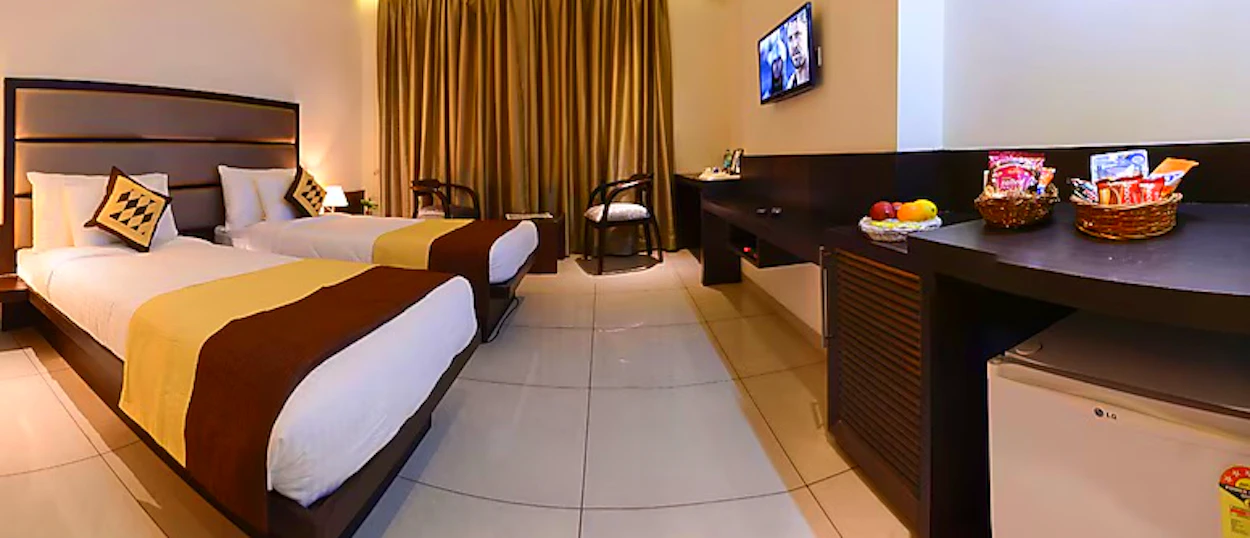 A well-appointed hotel room with two beds, a television, and a desk with snacks and fruit.